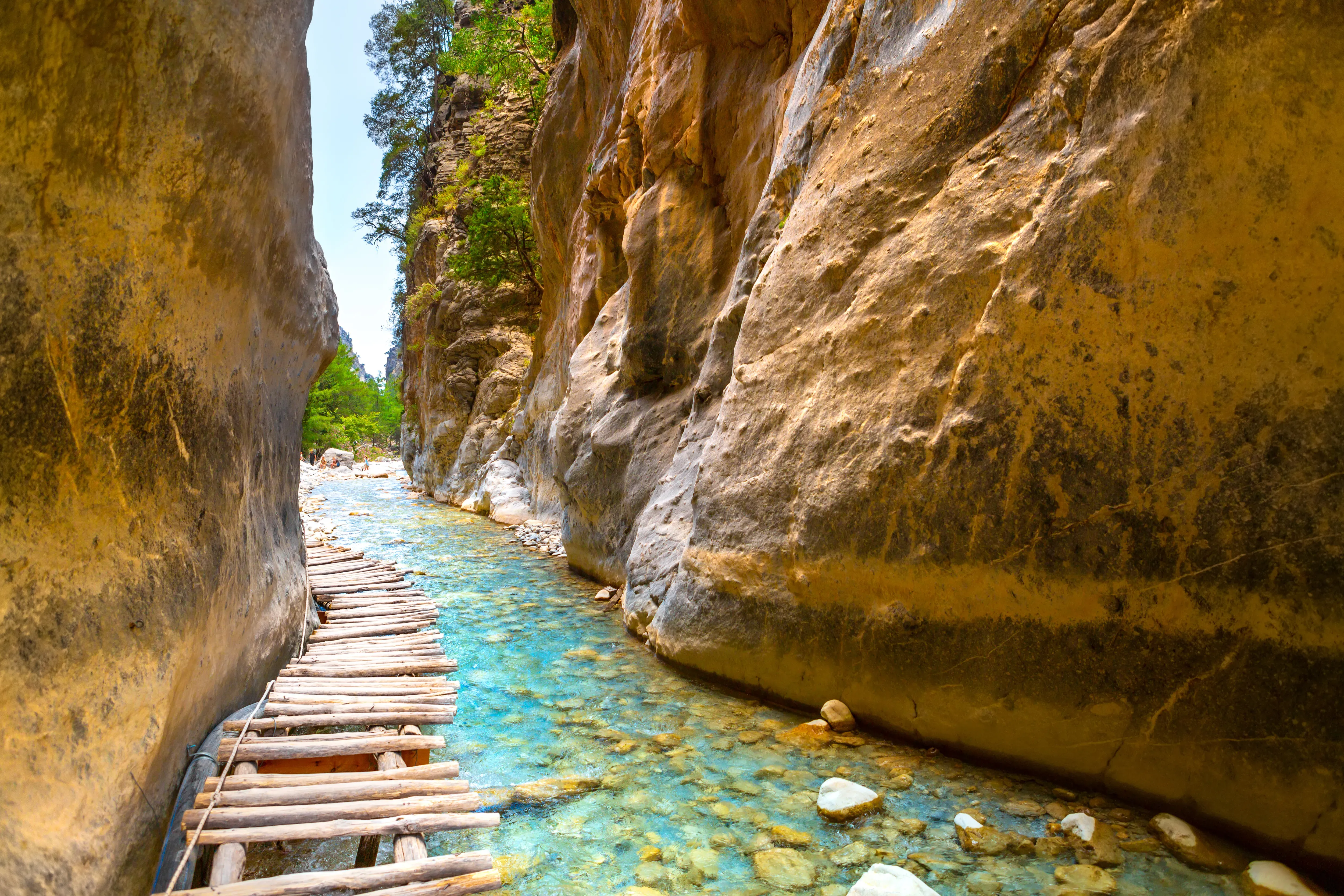  Schmale Schlucht mit Holzsteg dazwischen und Wanderweg &uuml;ber Flussbett mit klarem blauem Wasser.