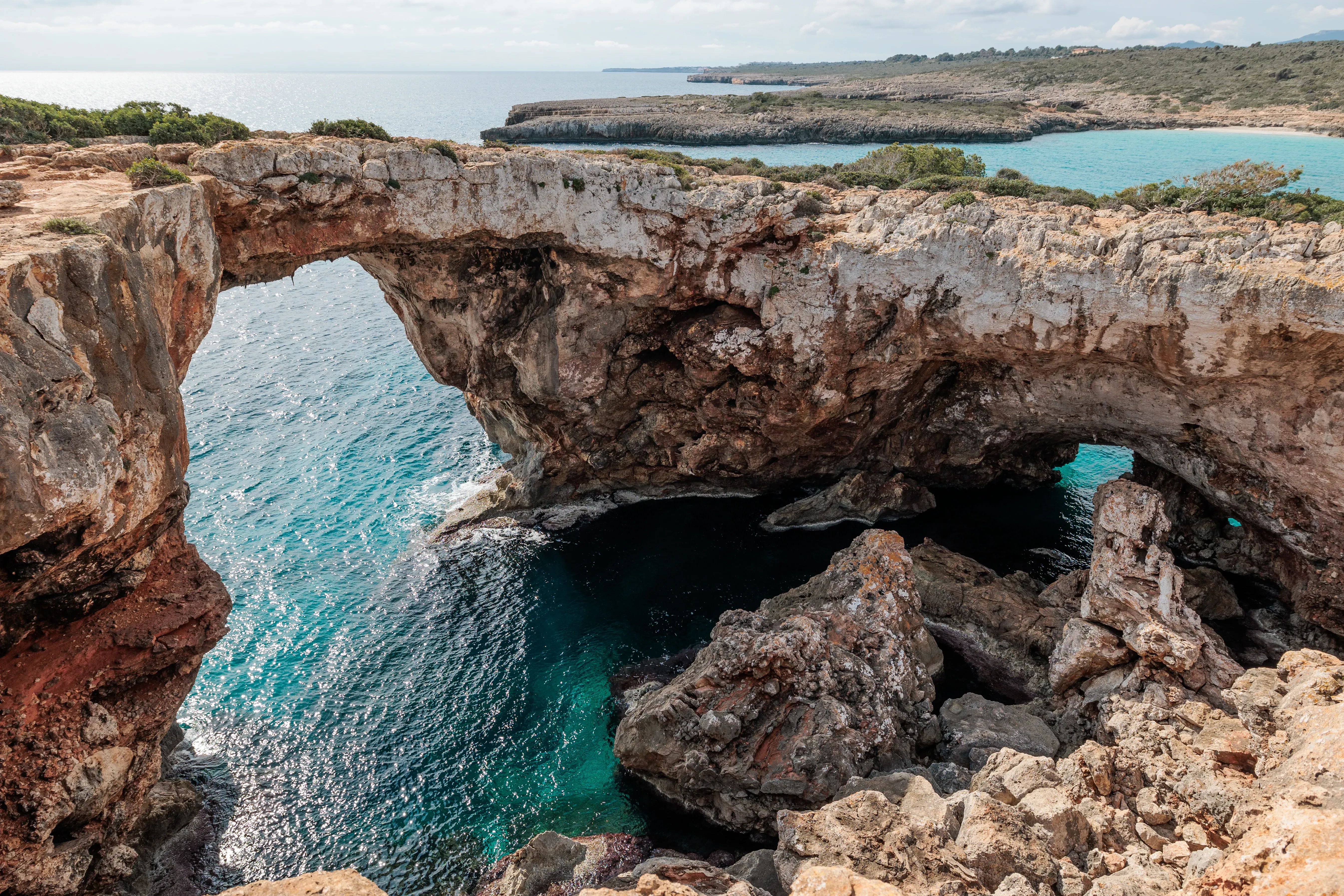 Kletterer hangelt sich an der Klippe entlang, unter ihm t&uuml;rkisblaues Meer