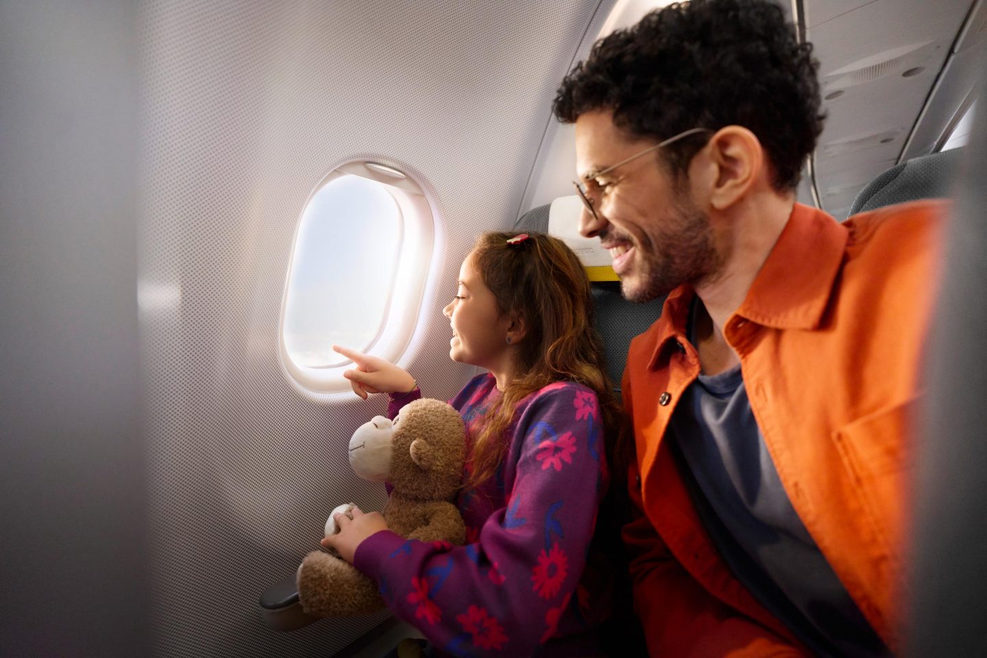 A father and his daughter look outside an aircraft window