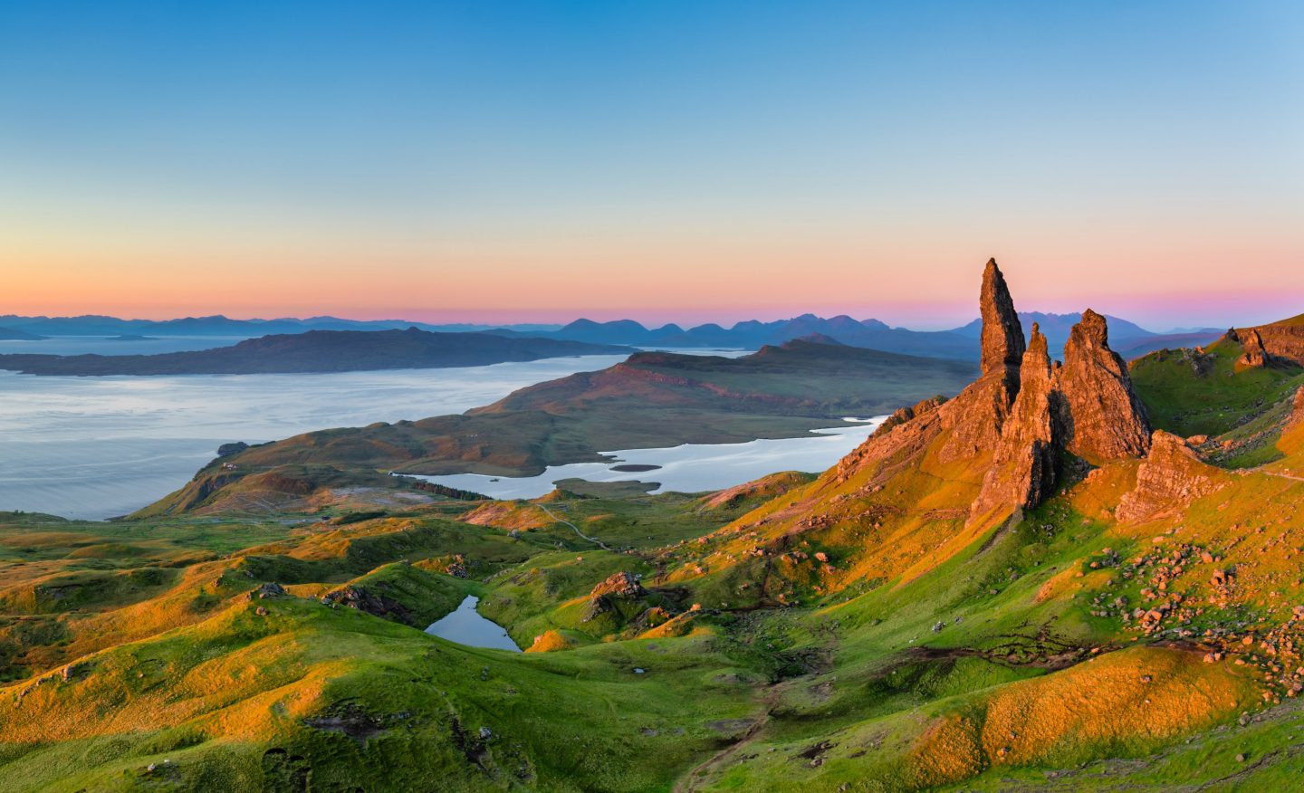 Old Man of Storr on Scotland’s Isle of Skye at sunrise, surrounded by green hills and lakes.
