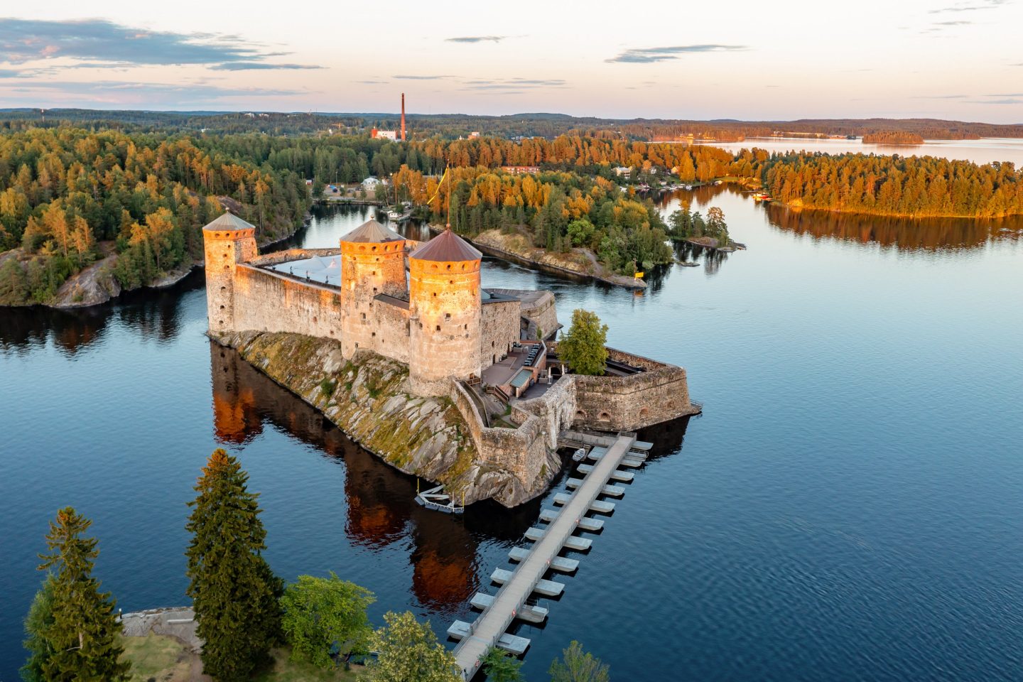 Aerial view of a historic stone castle on a small island, surrounded by calm water, forested shorelines, and numerous islands in Finland’s lake district.