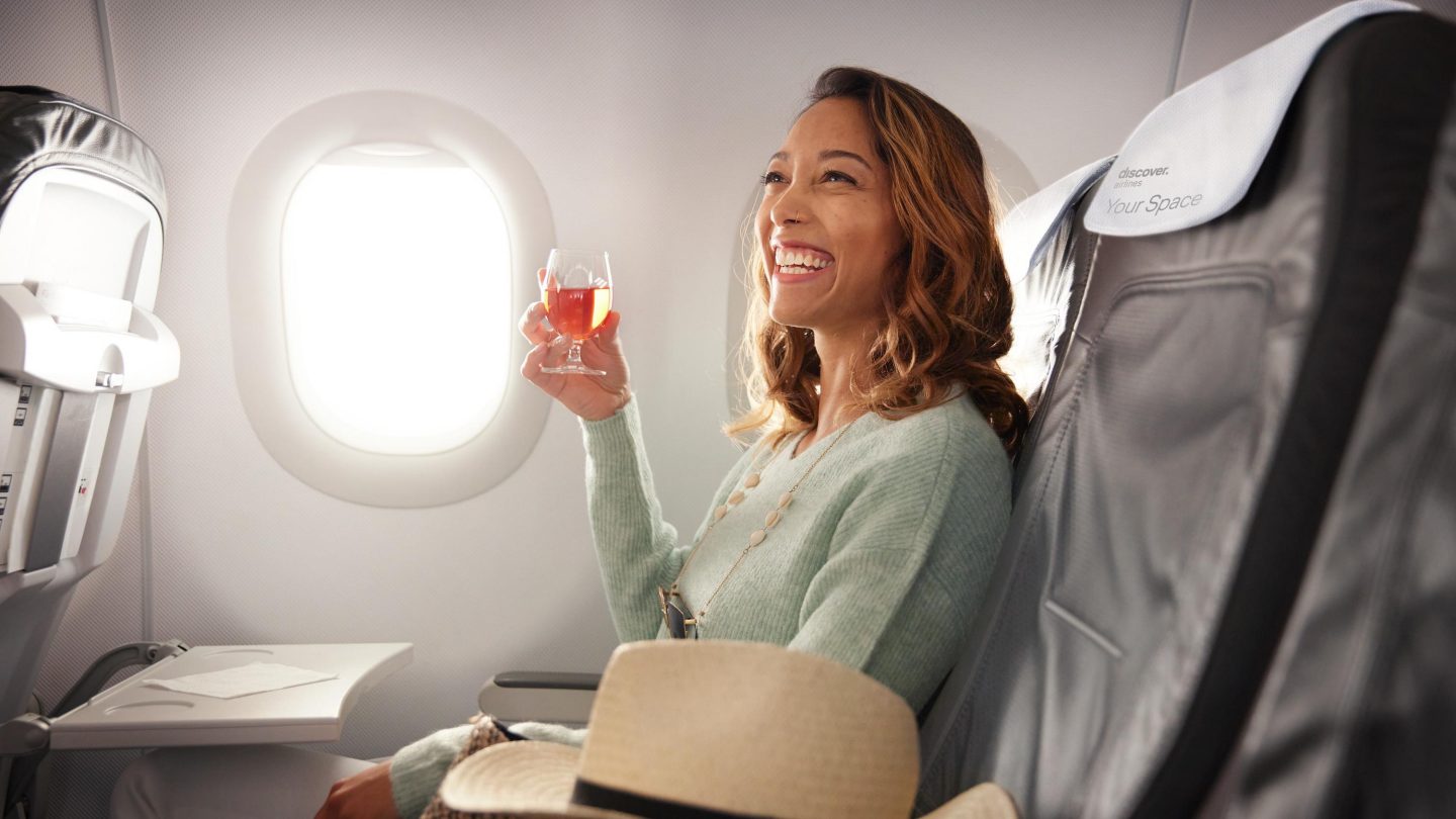 A woman is sitting in Business Class, drinking a glass of rosé