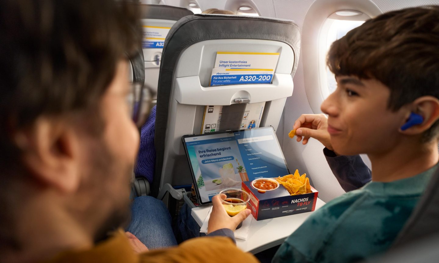 A boy is looking at the onboard cloud on his tablet and eating nachos.