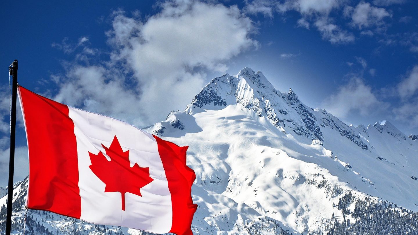 Mountains covered in snow with the Canada flag in the front