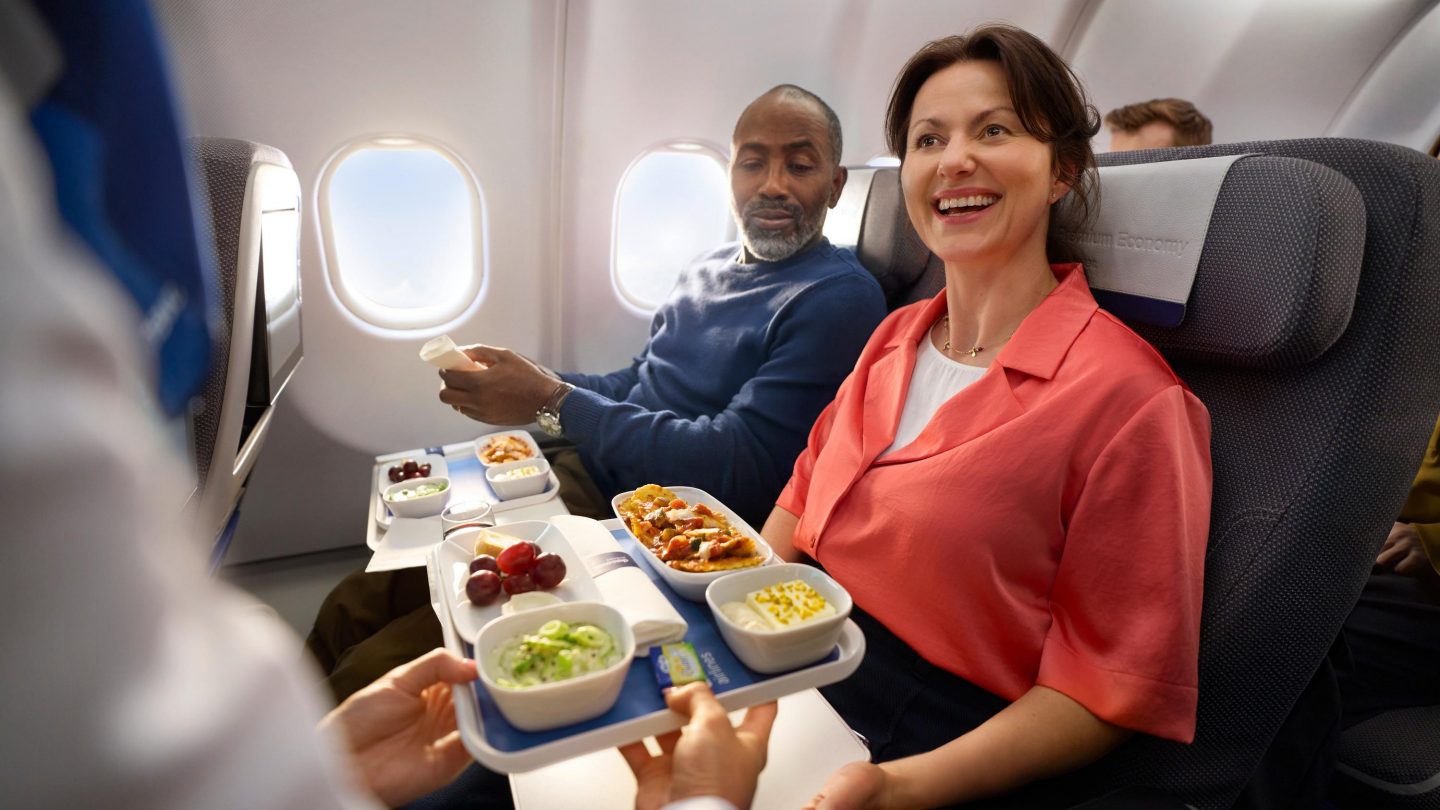 Two people are served food in Premium Economy Class