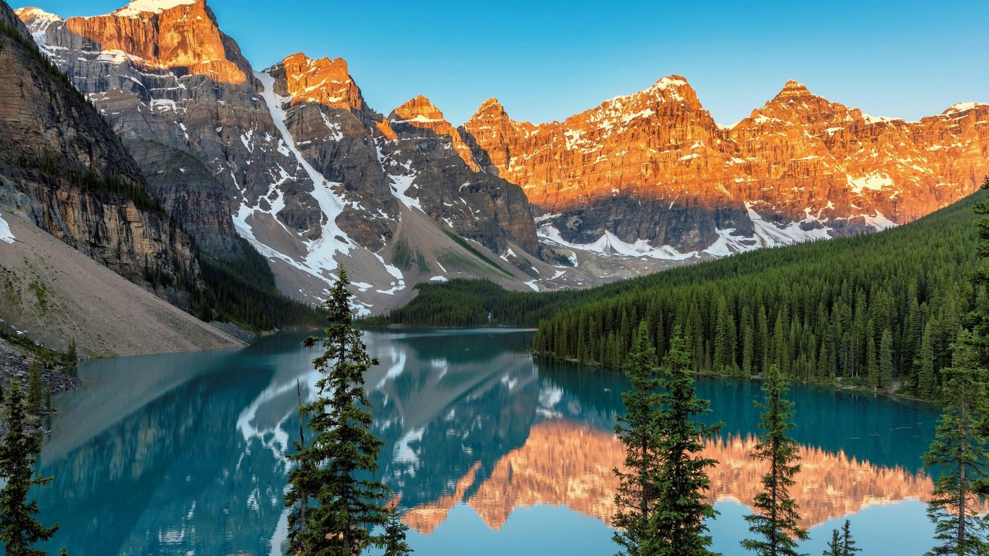 Turquoise mountain lake surrounded by snow-capped peaks in warm sunlight.