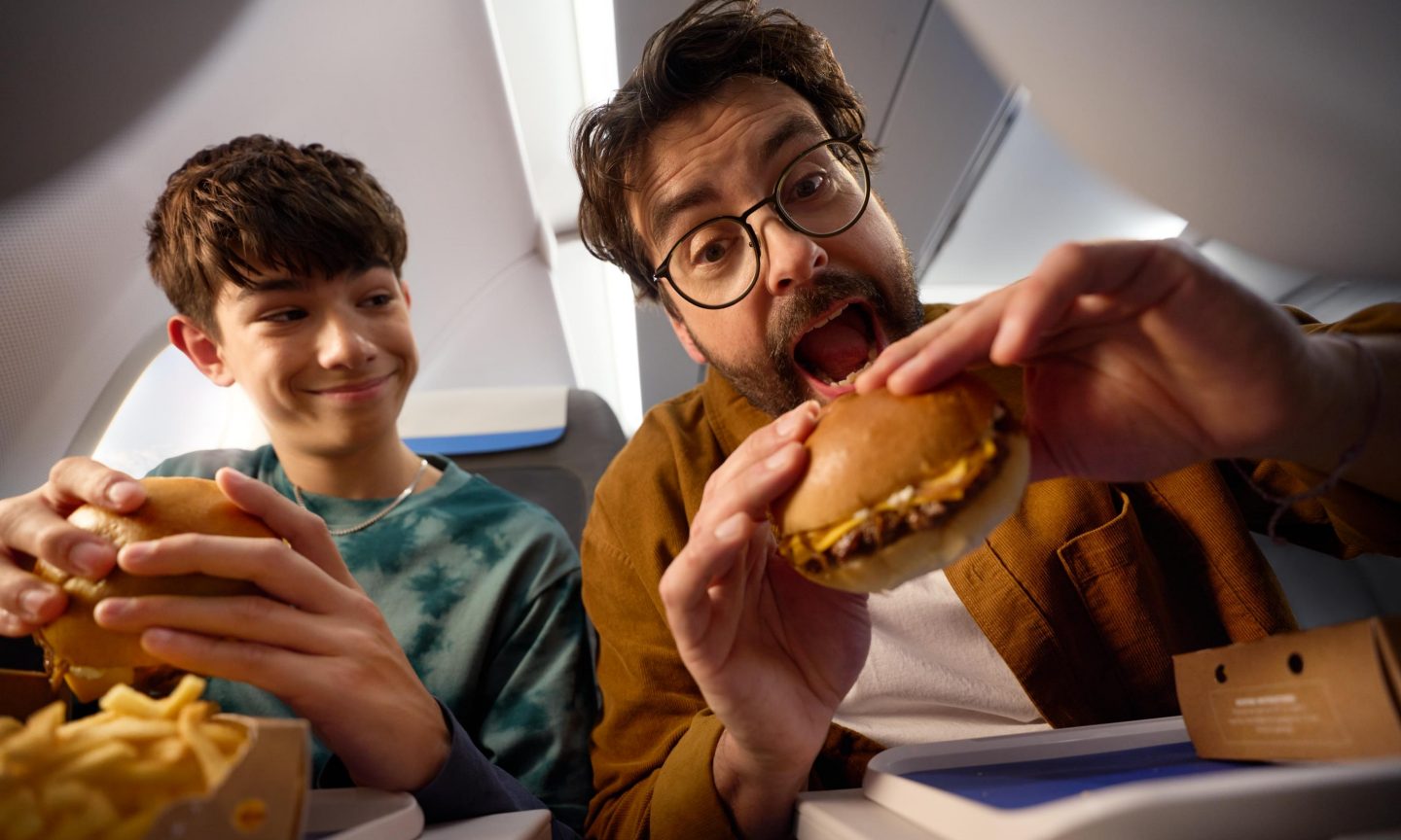 Vater und Sohn essen Smashburger mit Pommes in der Economy Class