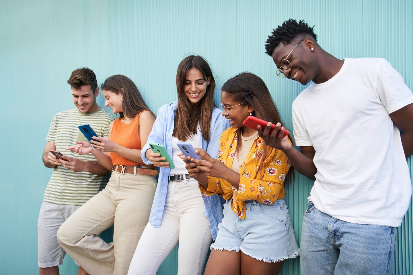 Eine Gruppe junger Menschen steht vor einer türkisen Wand und alle schauen auf ihre Smartphones