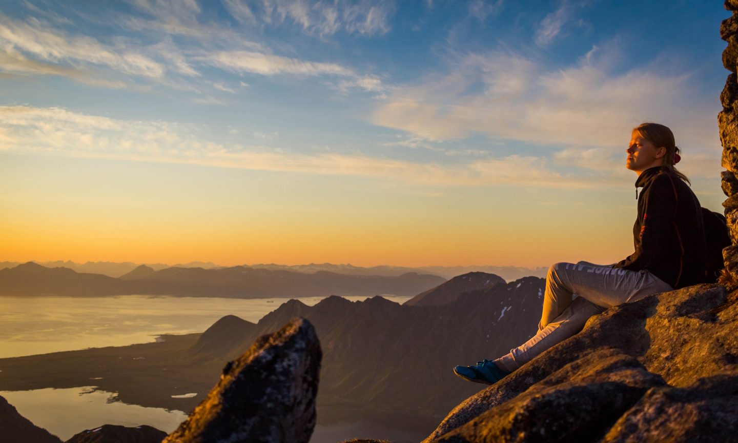 Person sitzt auf Bergspitze und schaut Sonnenuntergang an