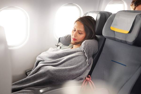 Frau schläft mit Decke in der Economy Class auf einem Langstreckenflug