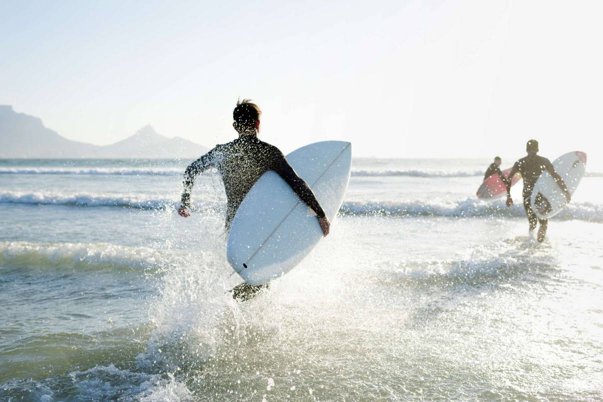 Ein Mann läuft mit einem Surfbrett unterm Arm in die Wellen