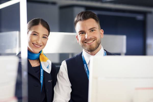 Mann und Frau in Discover Airlines Uniform stehen am Schalter und lächeln