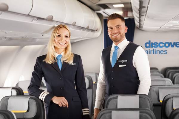 Discover Airlines Crew steht in der Economy Class und lächelt