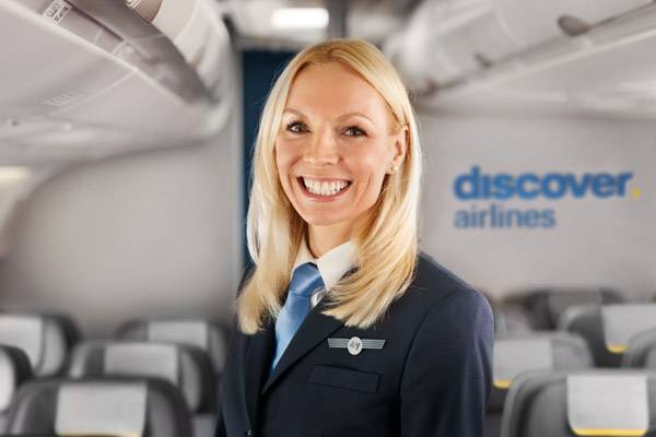 Discover Airlines Pilotin steht in der Economy Class und lacht