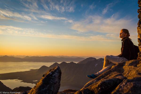 Person sitzt auf Bergspitze und schaut Sonnenuntergang an