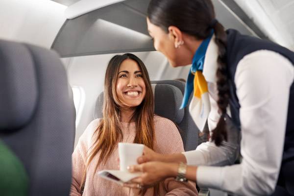 Frau wird von Flugbegleiterin in der Premium Economy Class bedient