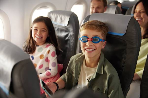 A girl and a boy sitting in an airplane laughing.